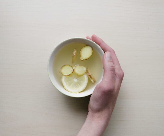 person holding white bowl with sliced lime and ginger inside